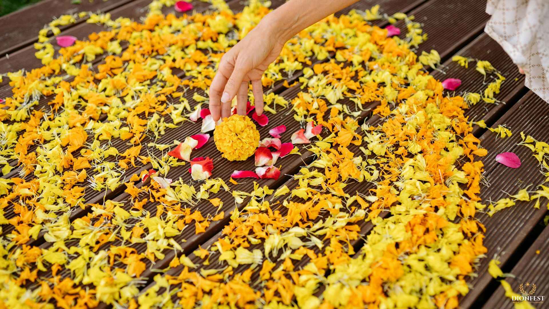 Hand placing marigold flower in a colorful Diwali rangoli made with petals