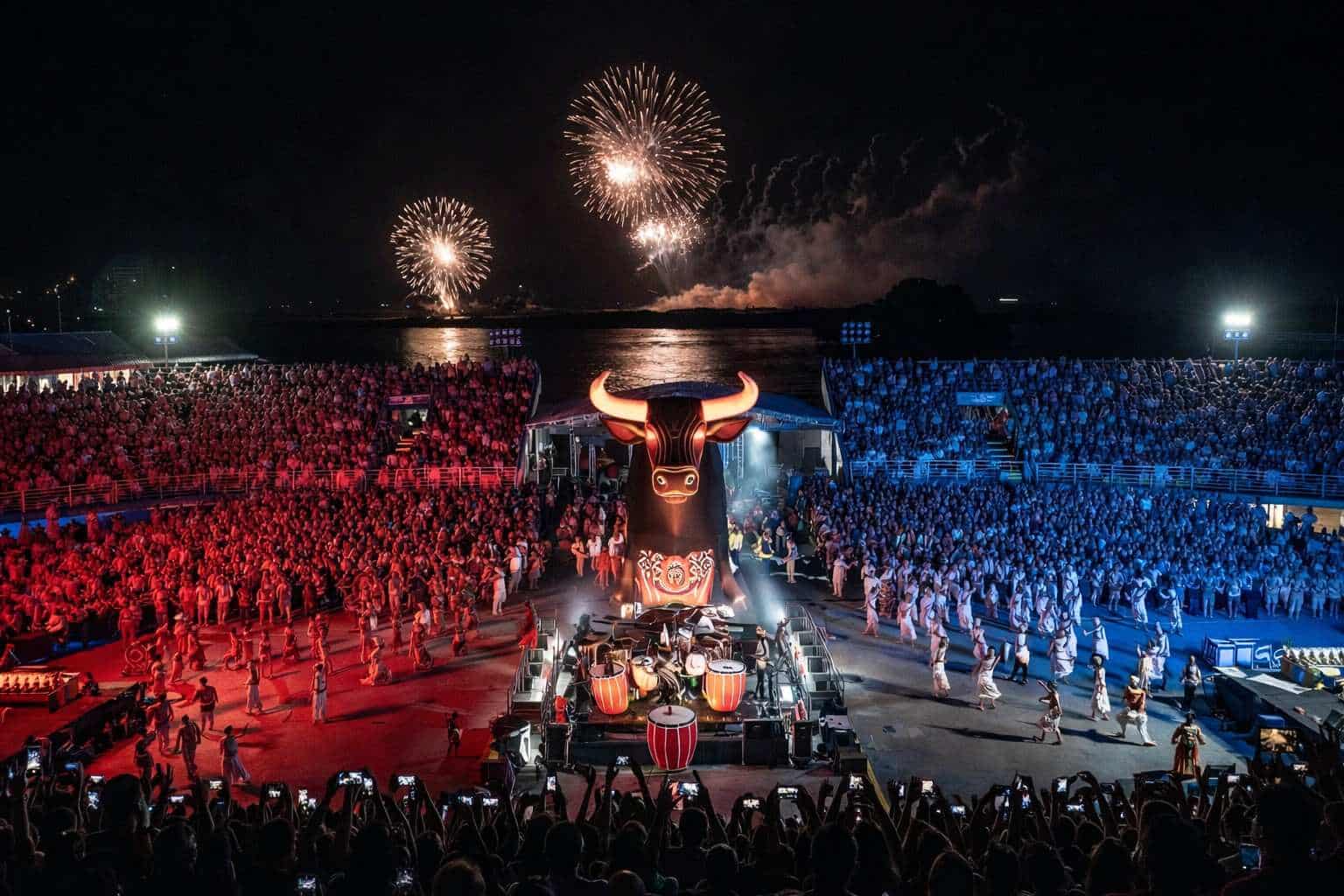 Nighttime Parintins Festival arena with giant bull float and fireworks over the Amazon River