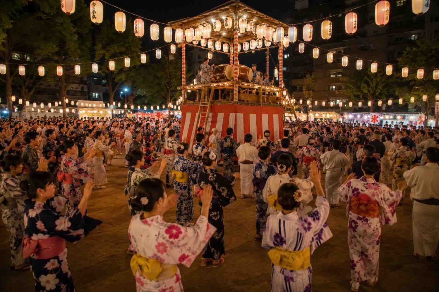 Crowd of people dancing Bon Odori in yukata around a wooden yagura stage during obon celebration