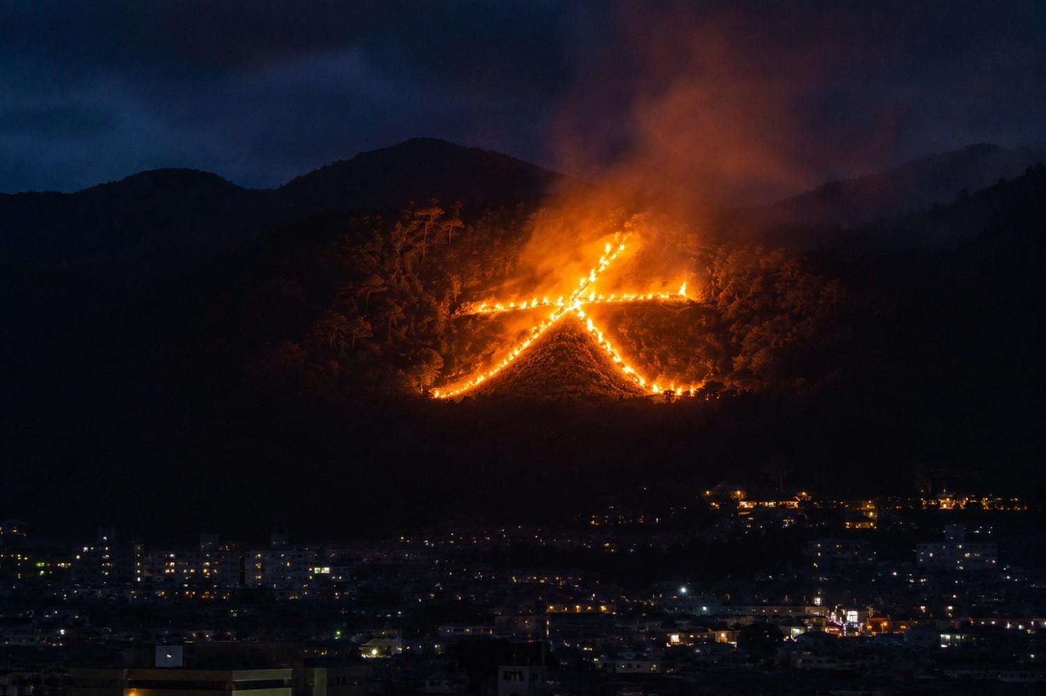 Giant Daimonji bonfire burning on a mountain above Kyoto city during obon festival at night