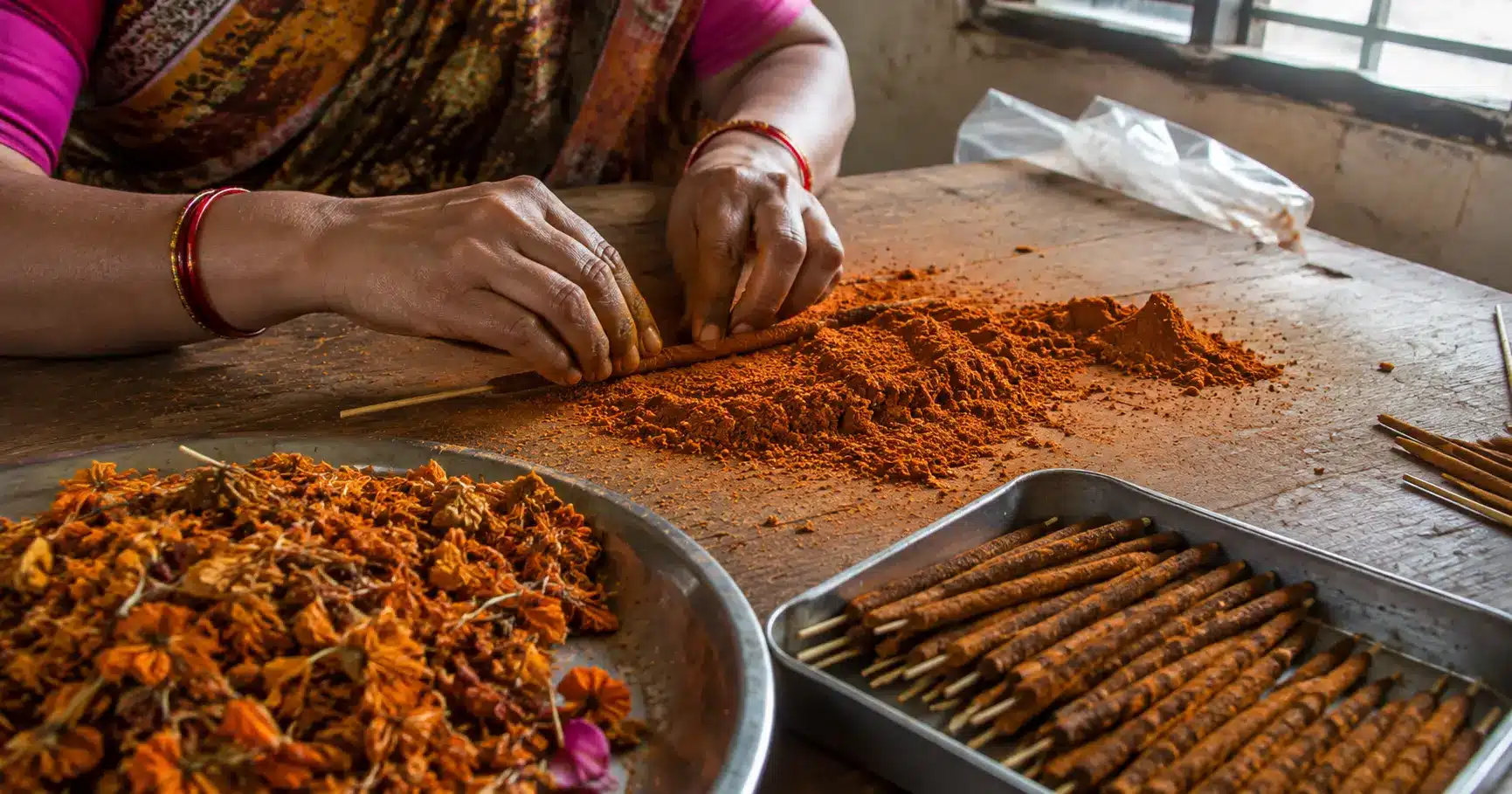 Woman hand-rolling incense sticks from dried recycled temple flower powder in a small workshop