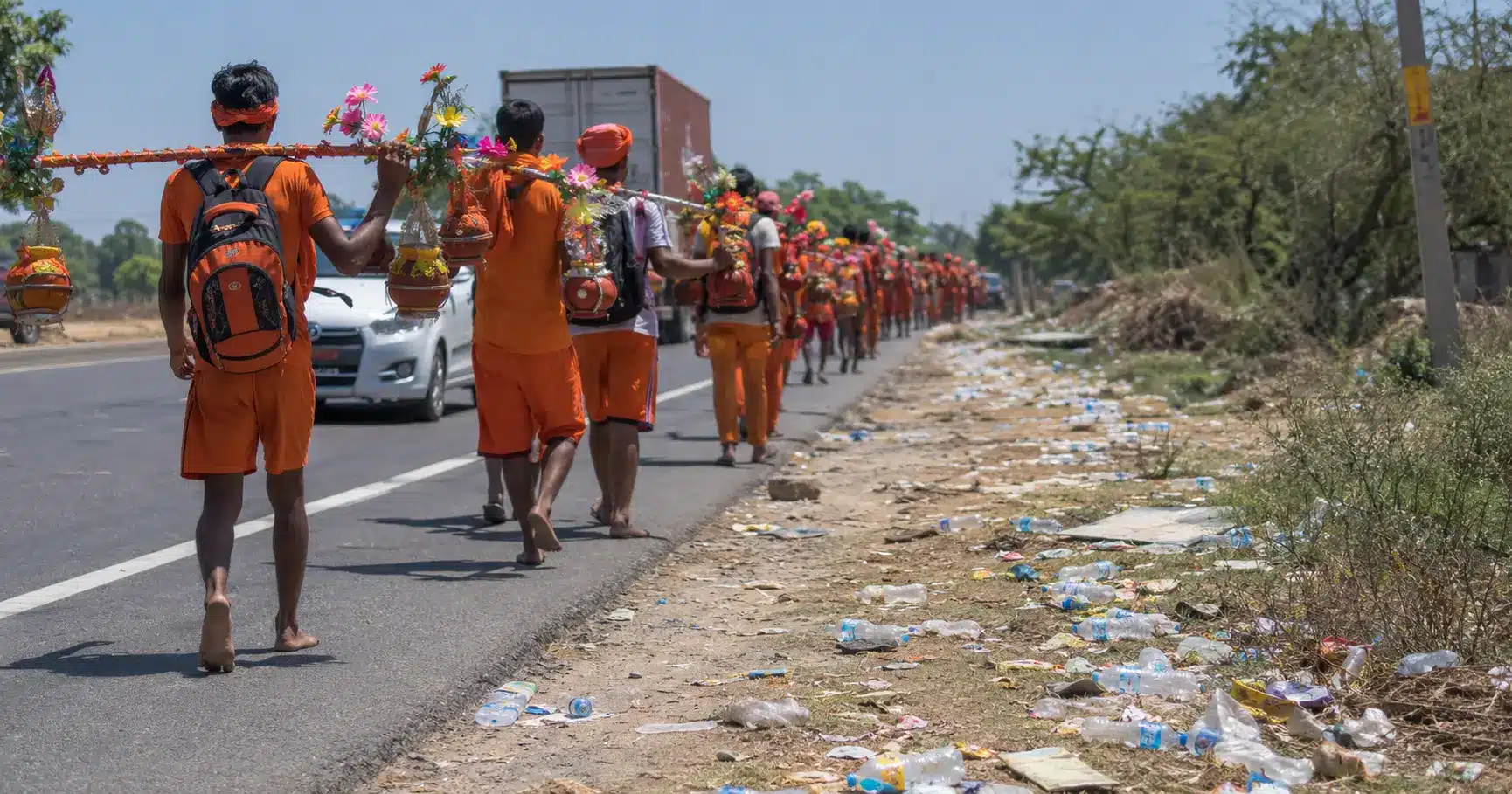 Pilgrims walking along a highway during a religious festival, with litter along the roadside