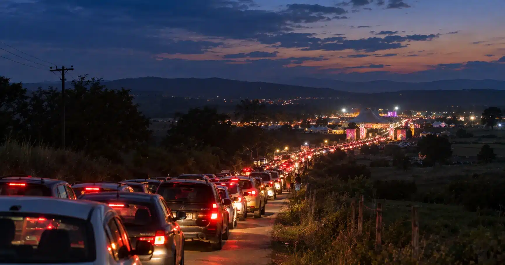 A long queue of cars backed up on the road to a festival at dusk