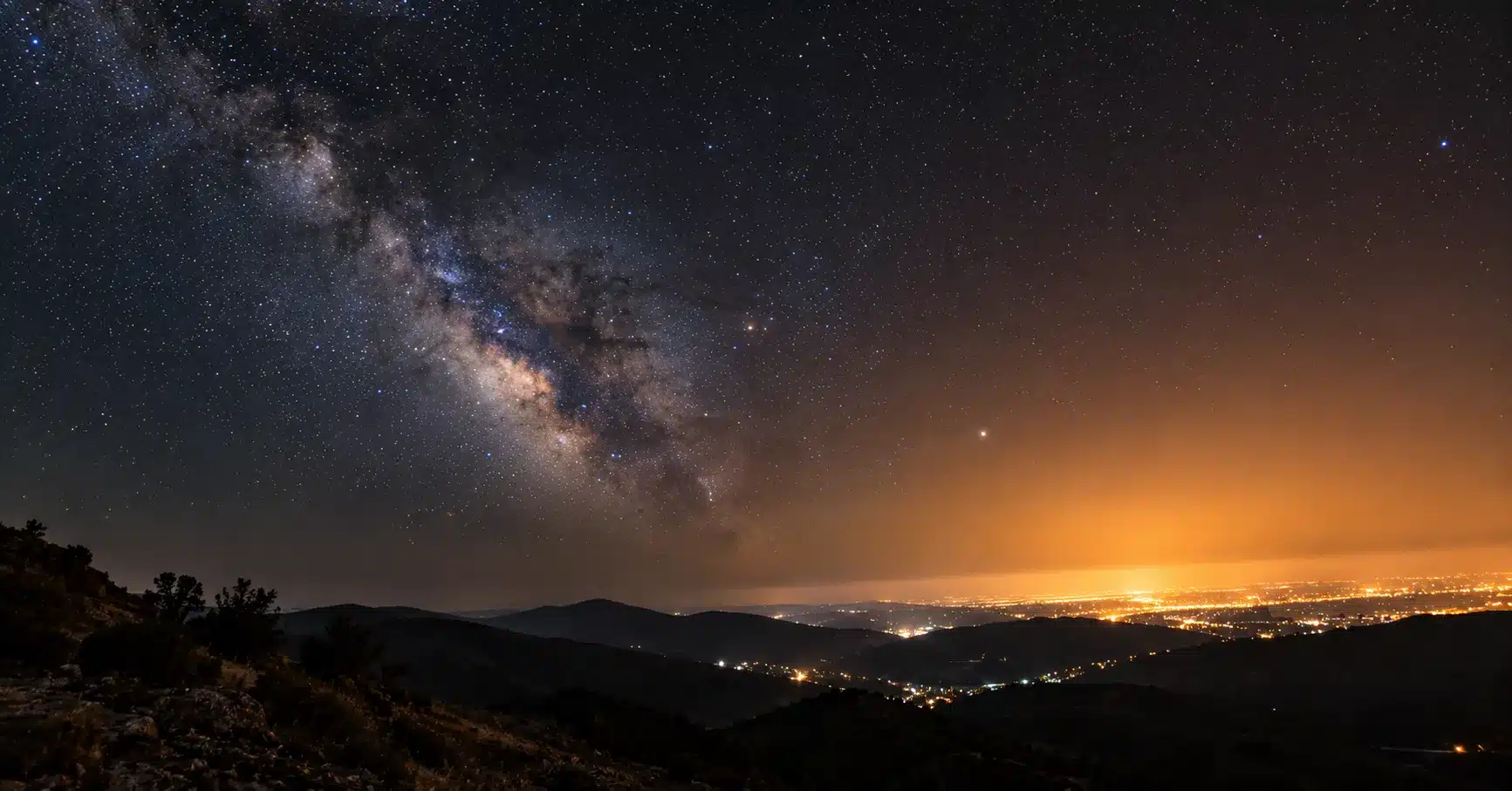 A star-filled night sky transitioning into an orange glow of light pollution on the horizon