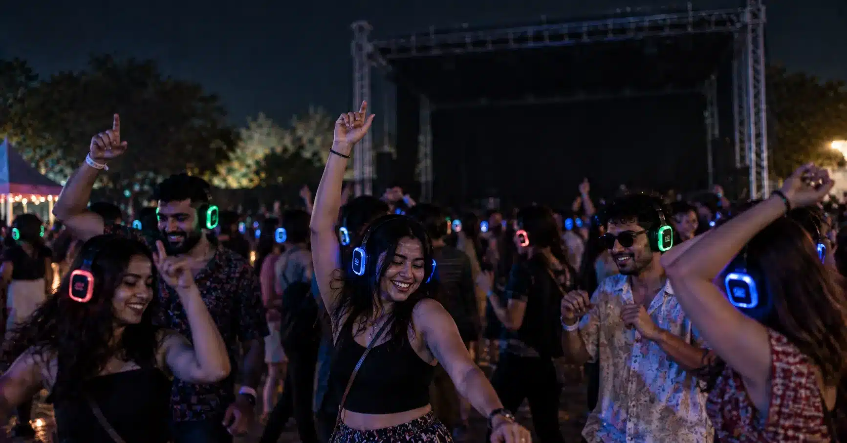 A crowd dancing outdoors at night wearing illuminated silent disco headphones