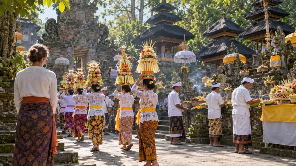 cultural festival etiquette: sarong.jpg Alt Text: Women in kebaya carry offerings through a Bali temple courtyard as a visitor in a sarong and sash watches