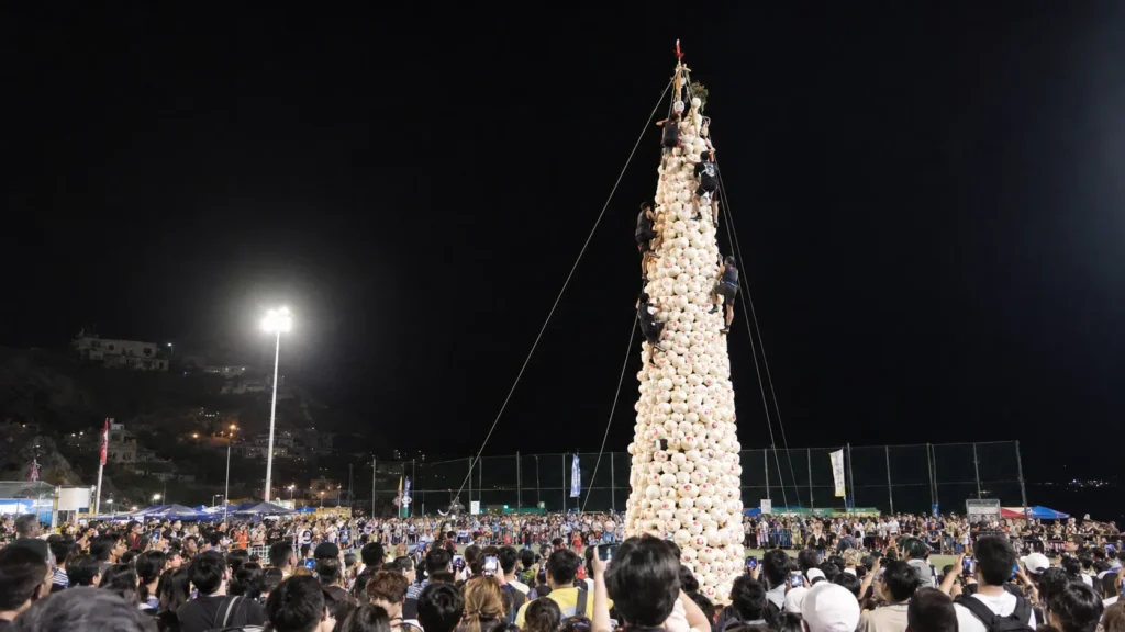 Climbers racing up a tower of white buns under floodlights at the Cheung Chau Bun Festival final