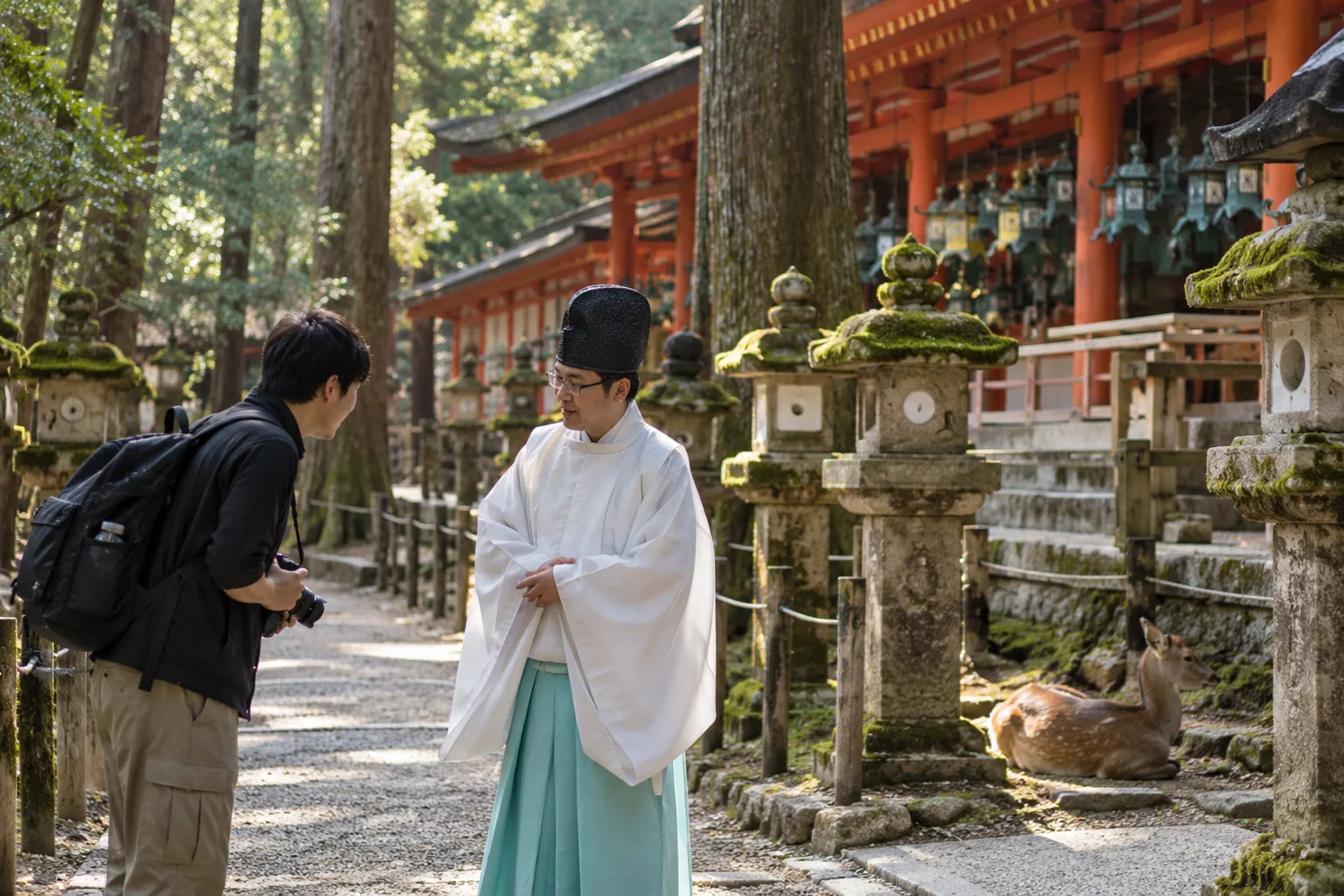 Visitor lowers a camera to ask a shrine priest for permission on a lantern-lined path at Kasuga Taisha, Nara